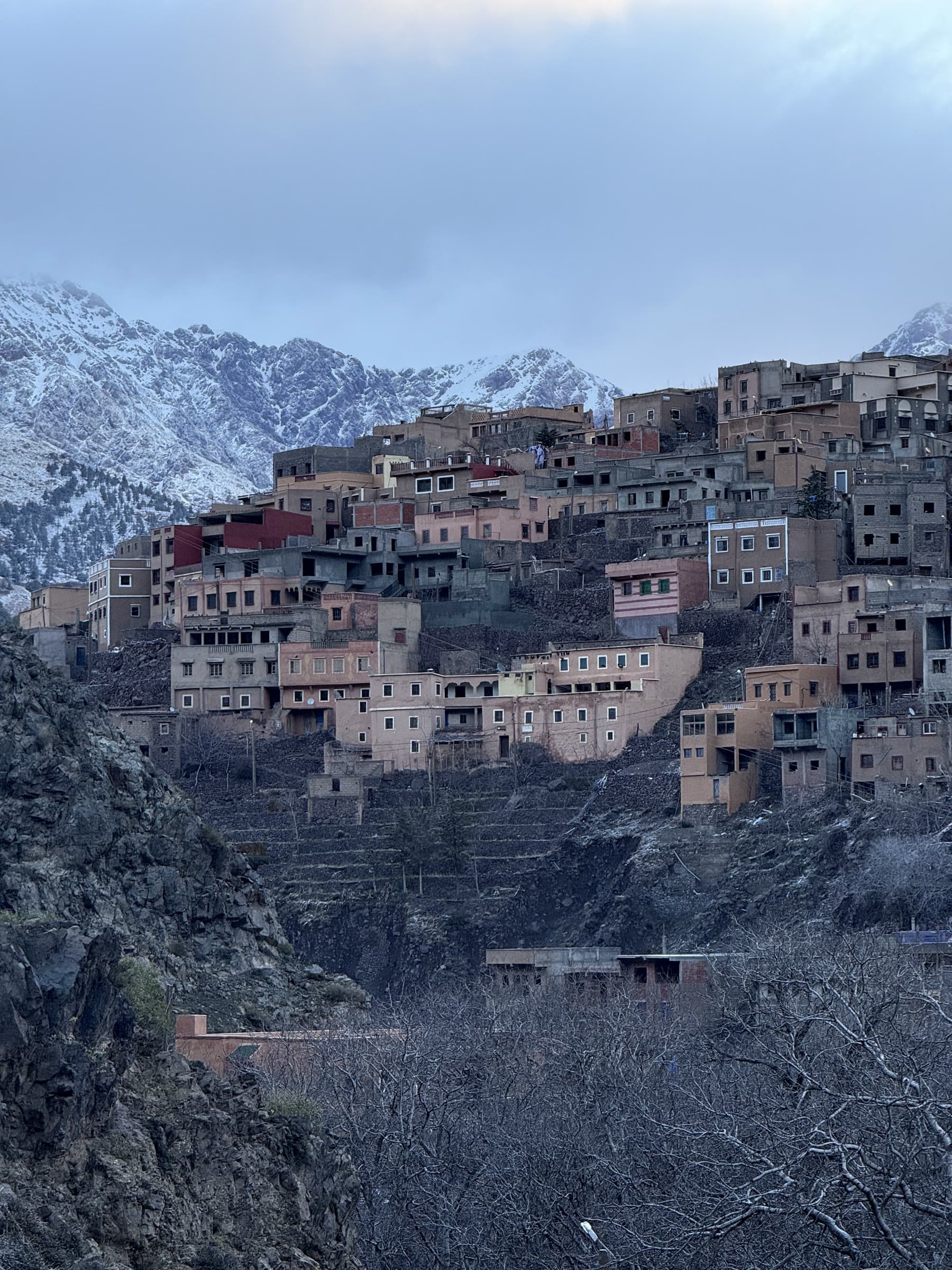 The village of Aremd stacked up its hillside at dusk, walnut terraces below and snow on the peaks behind