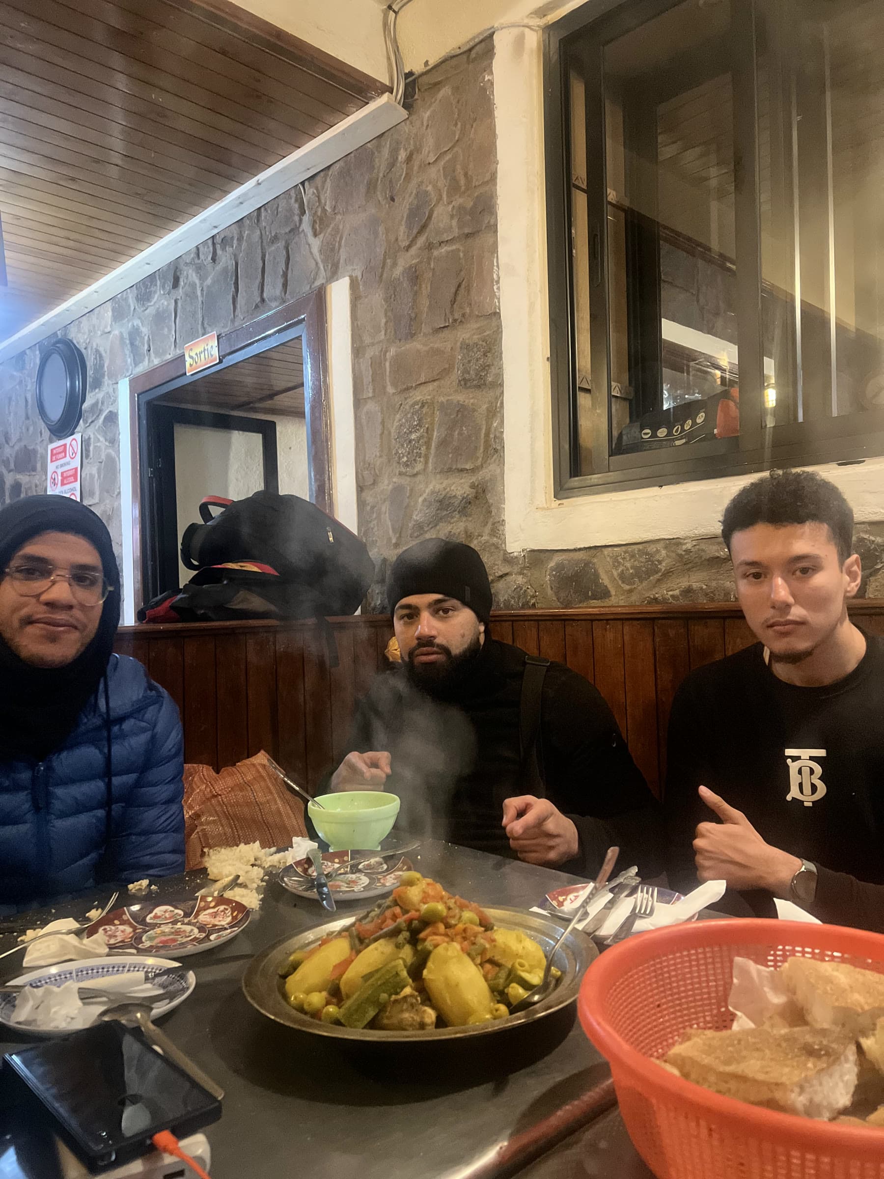 A vegetable tagine steaming on a table, three walkers sitting round it with bread and glasses