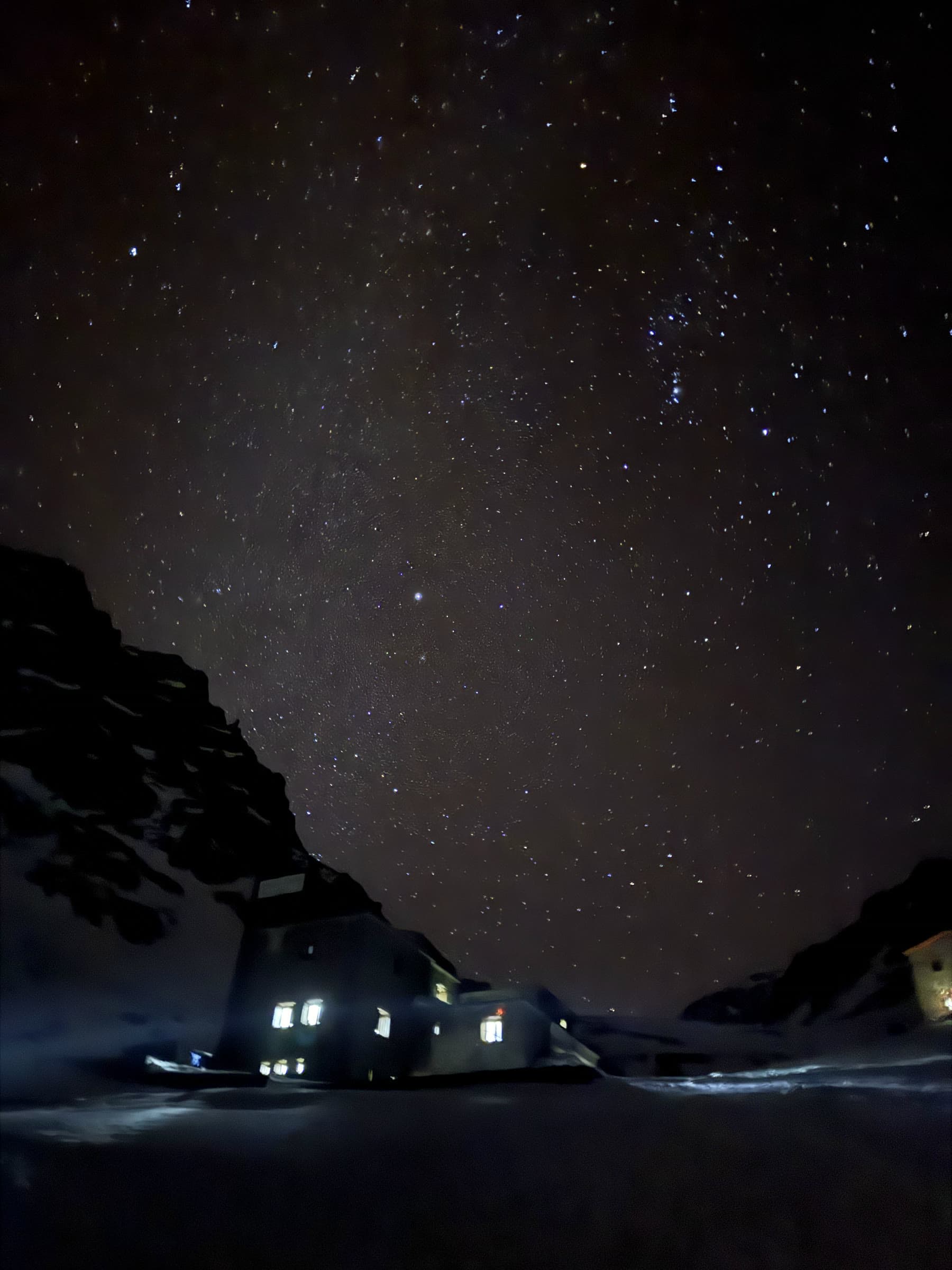The refuge at night with its windows lit, under a full field of stars
