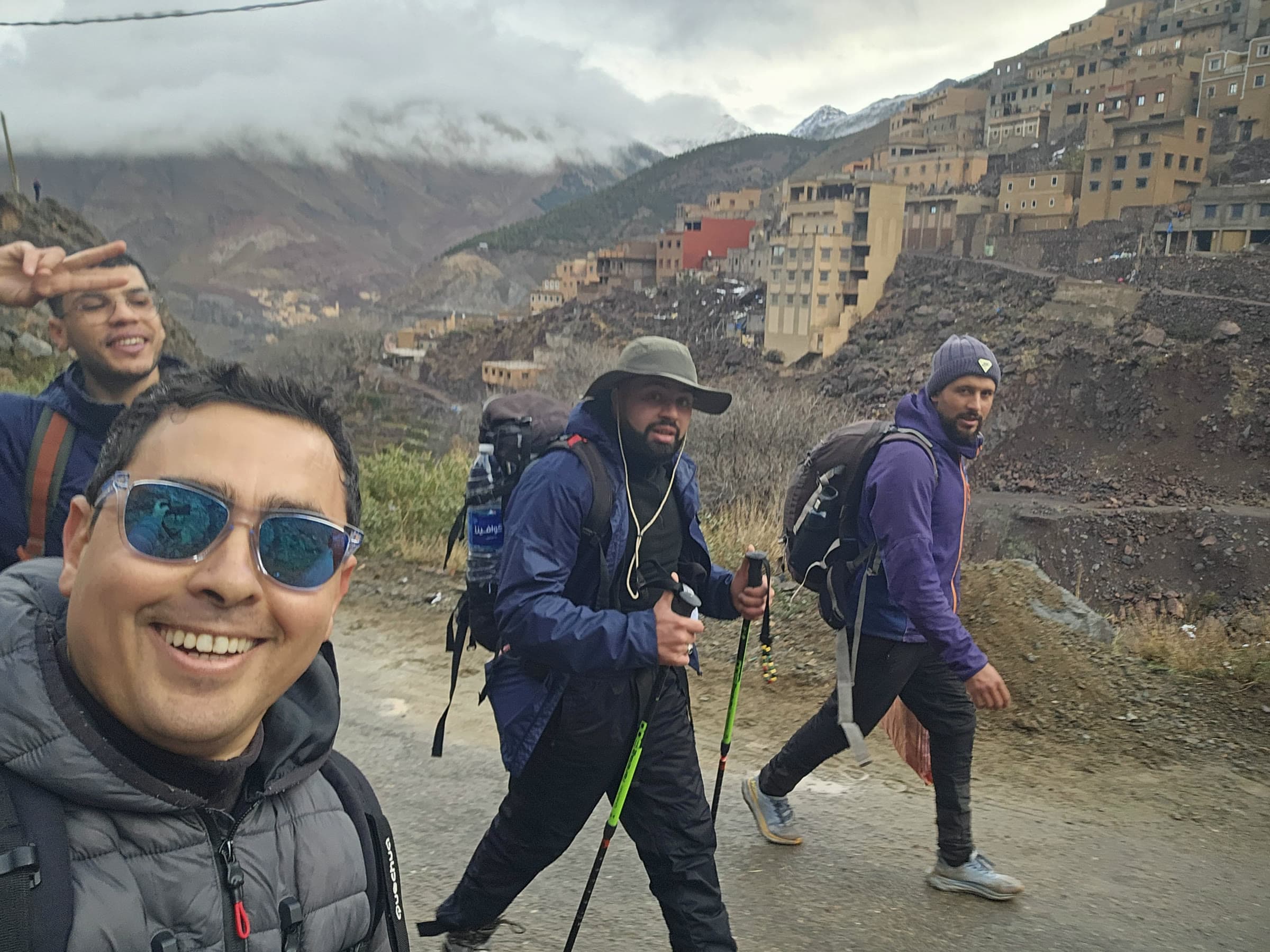 Four walkers on the road into the Aït Mizane valley, village houses climbing the slope behind them