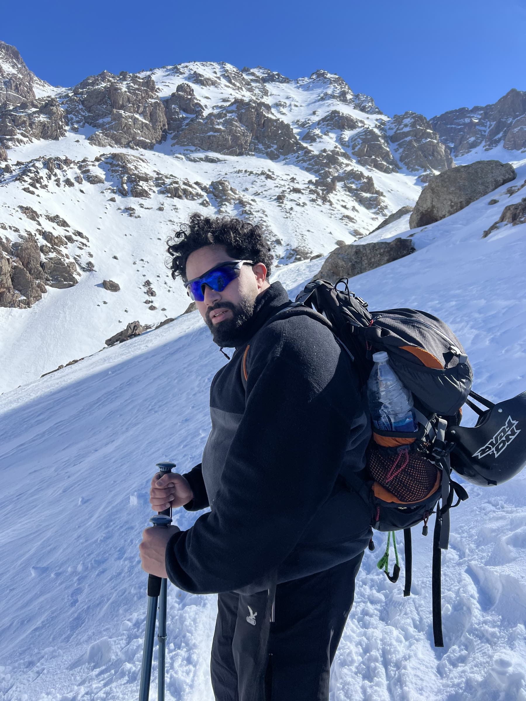 Zakaria Basraoui stopped on a snow slope below the summit ridge, poles in hand, looking back at the camera