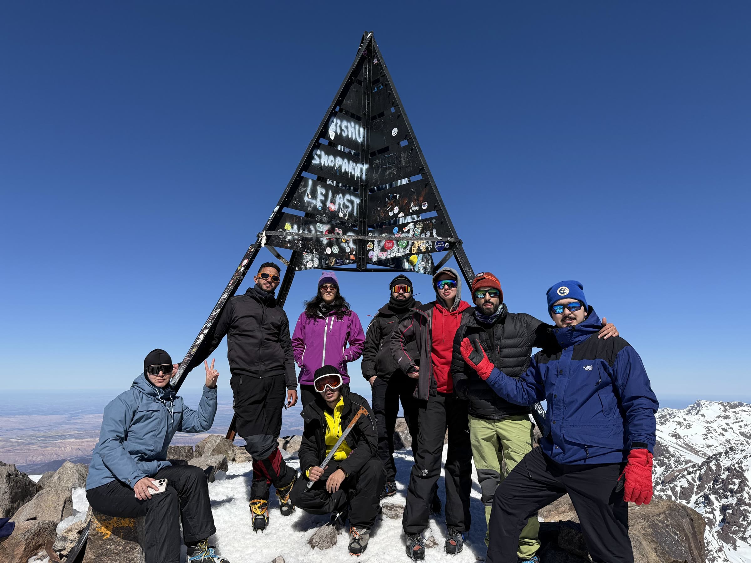 A group of eight at the Toubkal summit pyramid, the High Atlas dropping away behind them